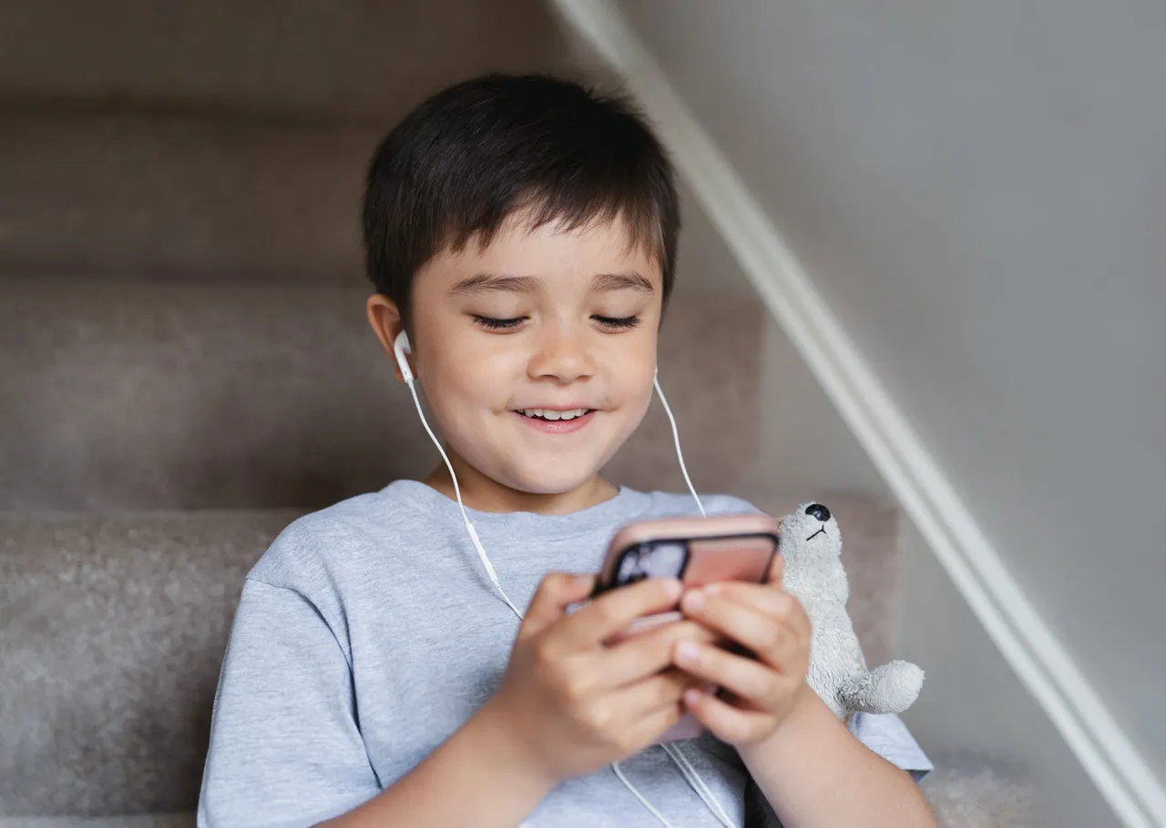 Niño jugando con un celular y audífonos