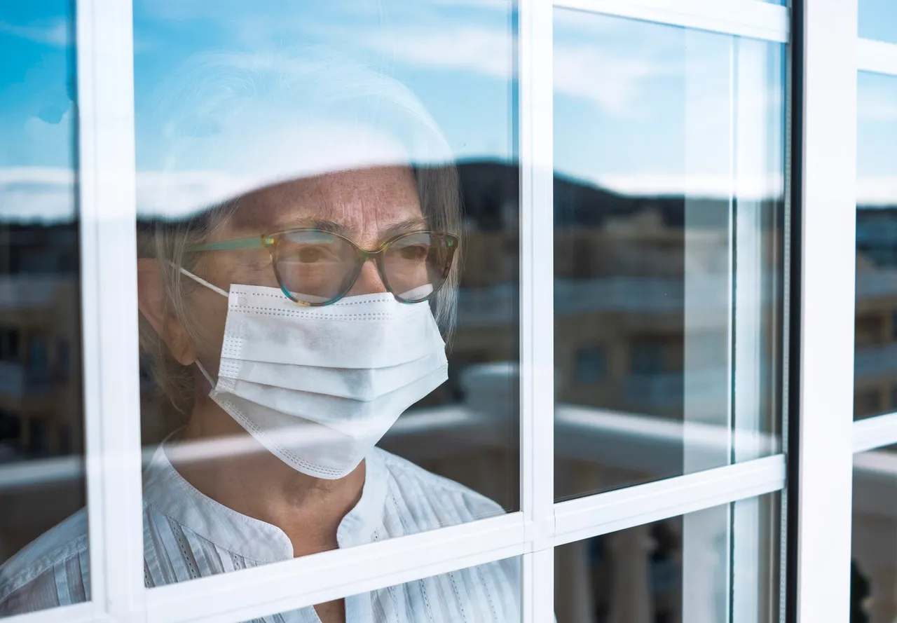Coronavirus pandemic, senior woman in self quarantine to avoid contagion of infection by virus covid-19. Stays home looking outdoor from the window. Prevention concept