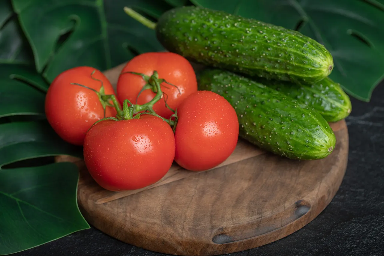 Pile of fresh organic vegetables. Cucumbers and tomatoes on wooden board with green leaves